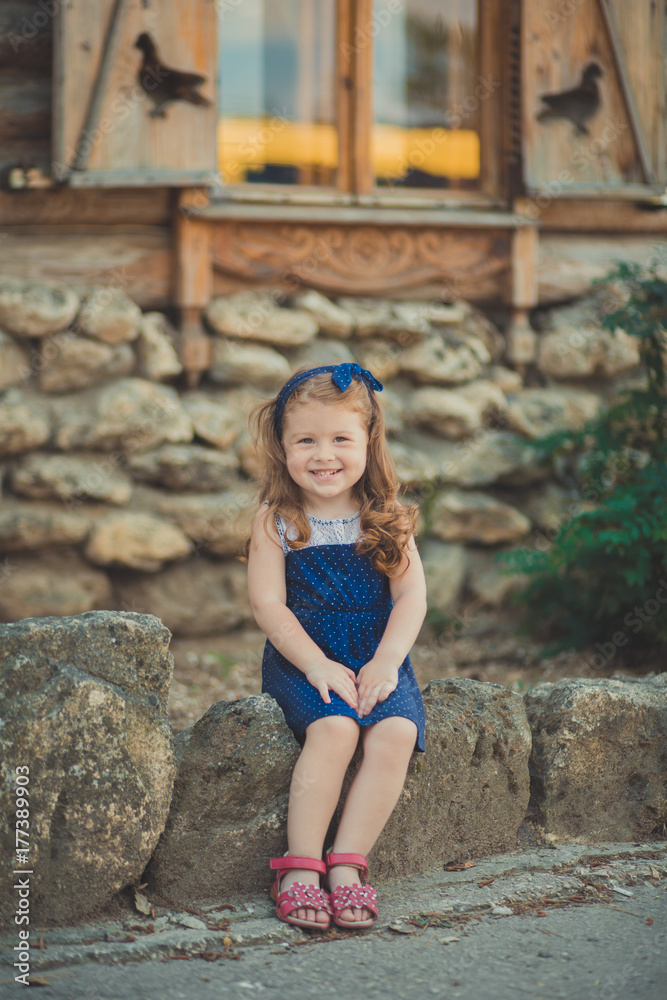 Young baby girl with brunette hairs and bright perfect skin cheeks wearing stylish awesome blue dress posing with bouquet of wild yellow flowers daisy