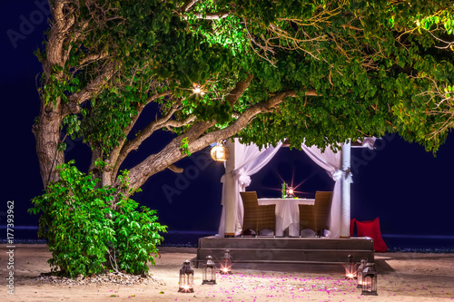 Gazebo for a romantic dinner with table and chairs. The path is fenced off with lamps with burning candles in the shade of a tree, at the sea, at night. Gili Trawangan island, Lombok, Indonesia.