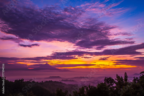 Mysticism and fog during sunrise over Candi Borobudur. Incredible colorful clouds of pink, the sky is yellow in blue. Sunrise in Jawa Tengah, Indonesia. View of Gunung Merbabu. photo