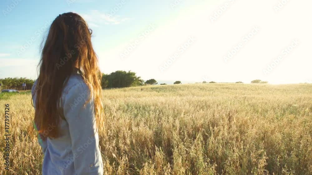 Beautiful girl walking and upping her arms in a wheat field with the sun behind Beautiful girl walking and upping her arms in a wheat field with the sun behind