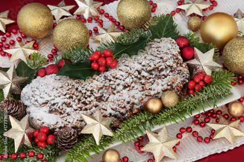 Chocolate stollen christmas cake on a plate with gold bauble and bead decorations, holly, fir and ivy.
