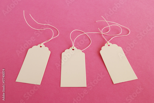 Three white blank paper price tags or labels set on the pink background.