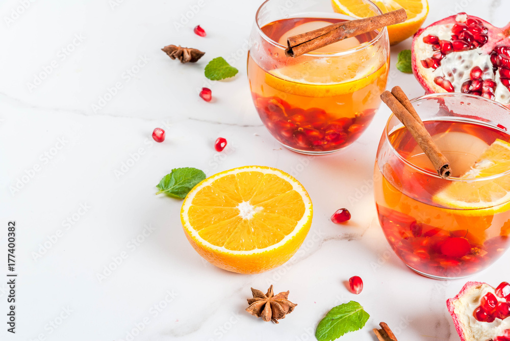 Fall and winter drinks. Warm refreshing cocktail with pomegranate, oranges, cinnamon, spices and mint. On a white marble table. Copy space Fall and winter drinks. Warm refreshing cocktail with pomegranate, oranges, cinnamon, spices and mint. On a white marble table. Copy space