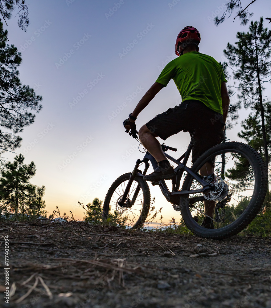 Mountain biker looking at sunset, bike trail in autumn mountains