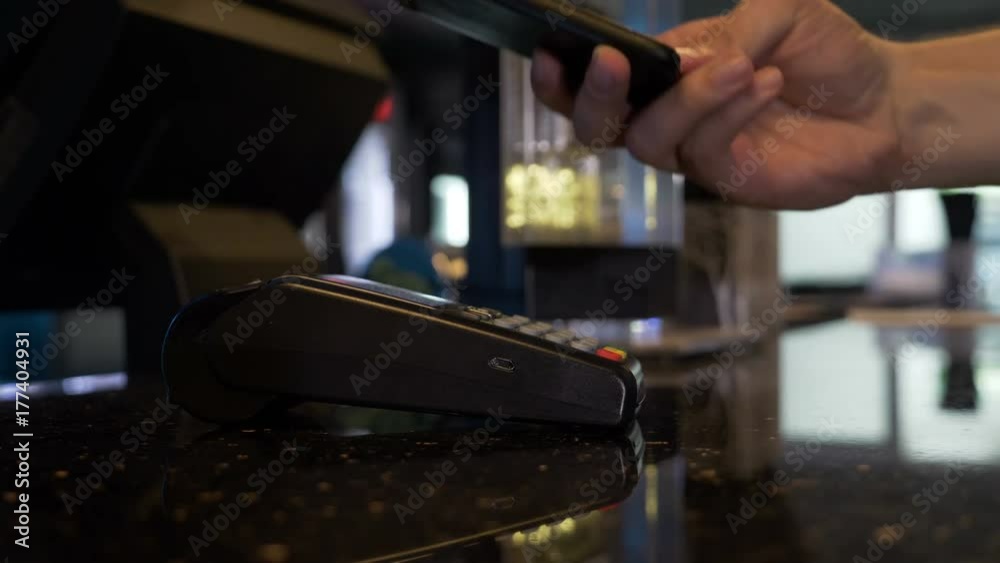 Closeup of man paying with bitcoin contactless with smartphone and terminal pos