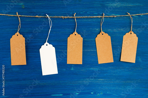 Five brown and white blank paper price tags or labels set hanging on a rope on the blue wooden background.