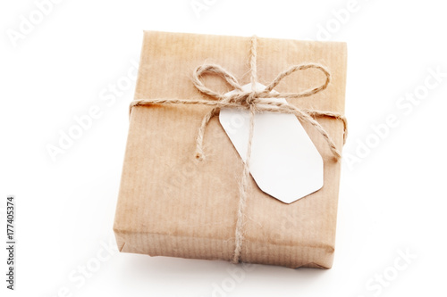 Gift box wrapped in craft paper with a label. Isolated present with a tag on the white background