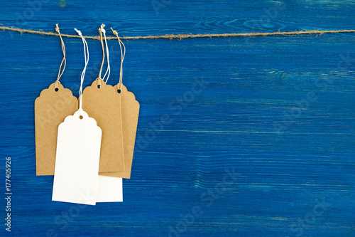Brown and white blank paper price tags or labels set hanging on a rope on the blue wooden background.