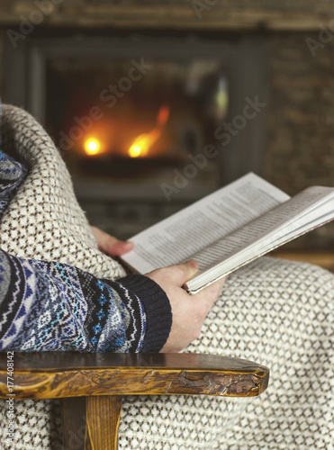 Man reading a book, sitting in a rocking chair with knit plaid in front of a fireplace