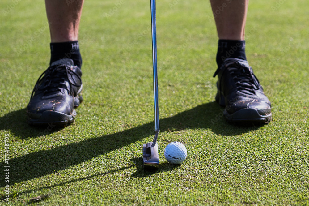 Obraz premium Putting a golf ball with a putter black shoes
