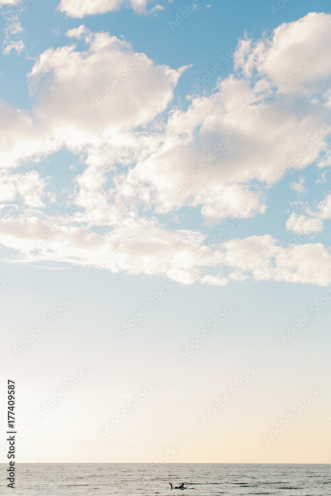 Surfer laying on surfboard floating between the waves during sunset Surfer laying on surfboard floating between the waves during sunset
