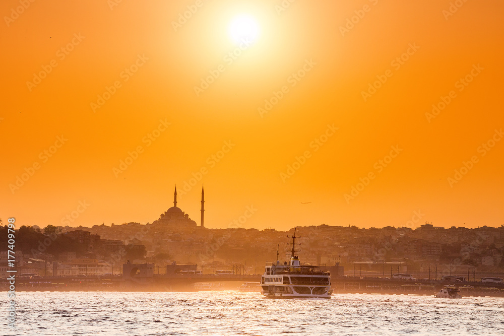 Passenger ferries and ships transport people through the Bosporus Strait in Istanbul at the background of a mosque and sunset