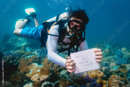 Scuba diver holding  Will you marry me? sign making unusual underwater marriage proposal
