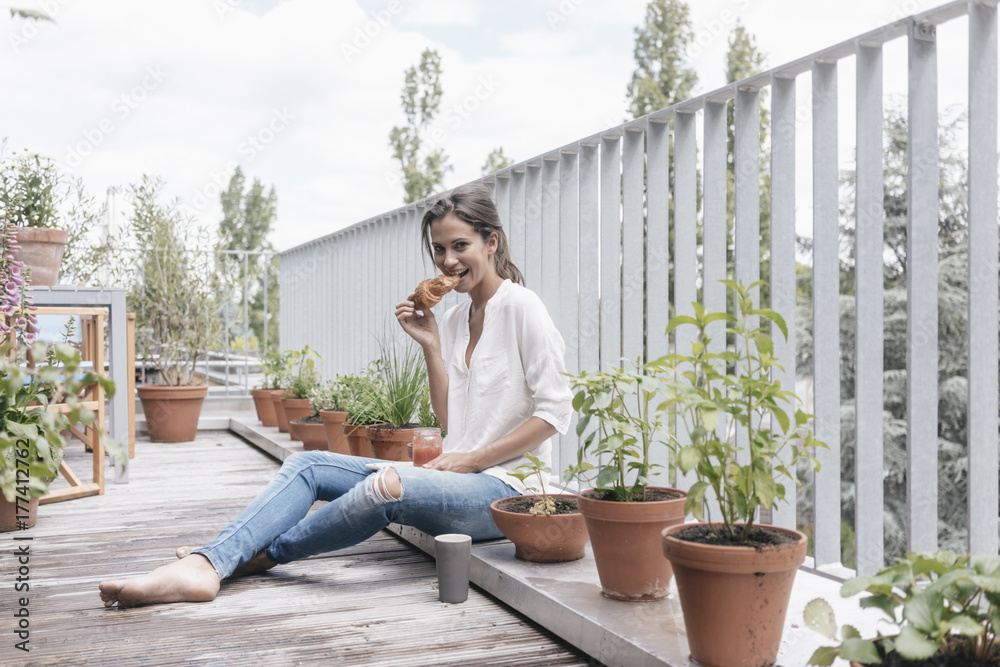 Smiling woman eating croissant with jam on balcony Smiling woman eating croissant with jam on balcony
