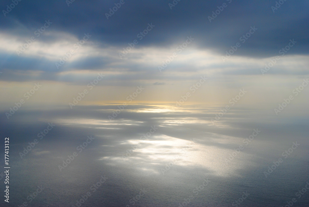 Sun shining at open sea through clouds making reflections at sea surface. Shot from airplane.
