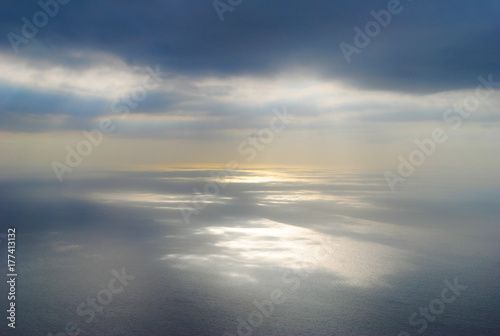 Sun shining at open sea through clouds making reflections at sea surface. Shot from airplane.