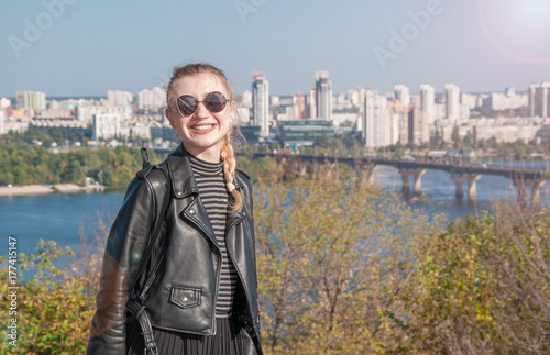 A beautiful blonde girl stands on the background of the city and smiles