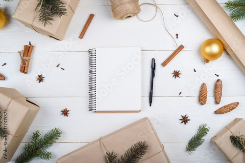 Top view of blank notebook for template design on white wooden background with xmas decorations, copy space. Christmas background with notebook for wish list or to do list, gift boxes. Flat lay