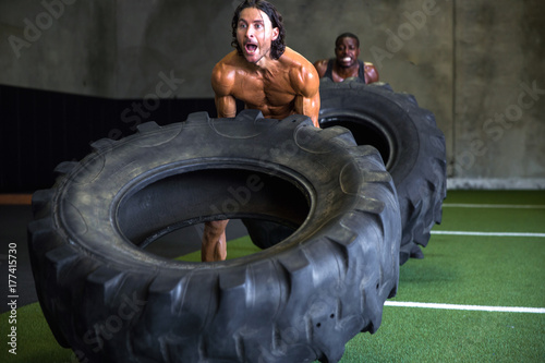 Male fit athlete pushes himself to lift heavy weight tire in a race for cross training