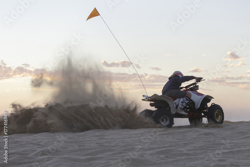 A woman riding a quad and kicking up sand photo