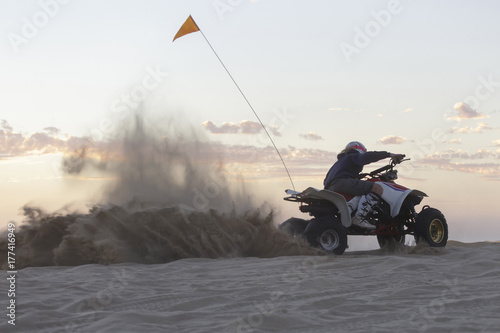 A woman riding a quad and kicking up sand