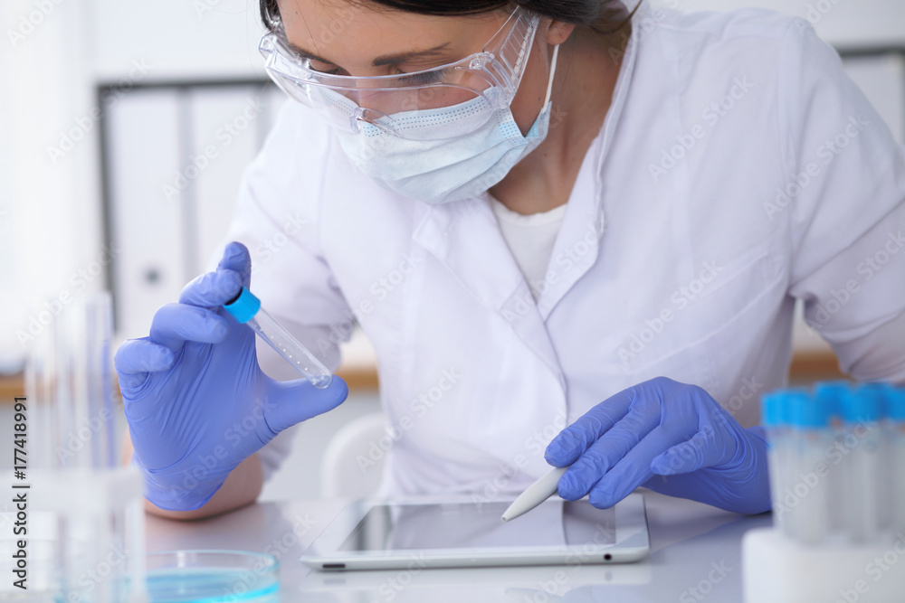 Close-up of professional female scientist in protective eyeglasses making experiment with reagents in laboratory. Medicine and research concept Close-up of professional female scientist in protective eyeglasses making experiment with reagents in laboratory. Medicine and research concept