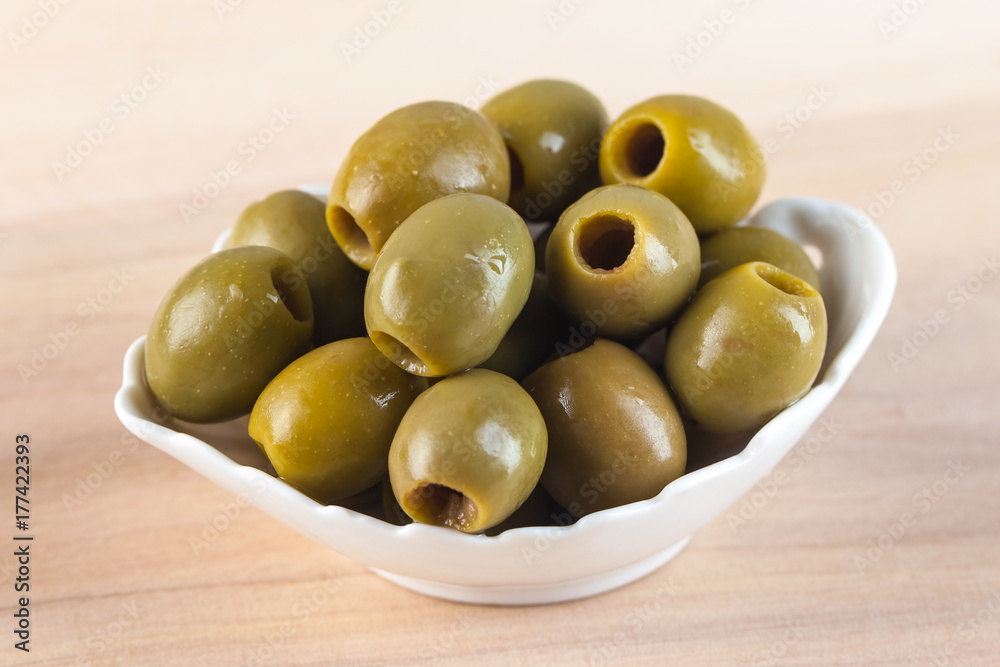 White bowl with green olives on wooden table White bowl with green olives on wooden table