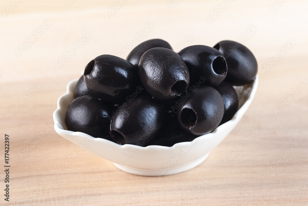 White bowl with black olives on wooden table