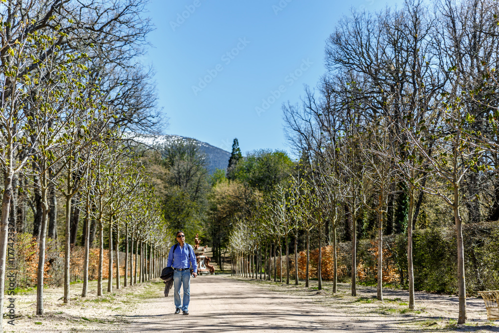 A man with a jacket in his right hand, walks along a great path of a park