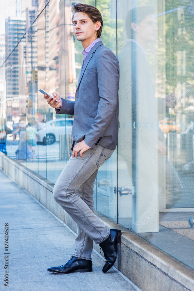 Young Professional Man wearing gray blazer, jeans, black leather shoes,  standing against glass wall on street in Manhattan, New York, texting on  cell phone, looking up, thinking. . Stock Photo | Adobe Stock
