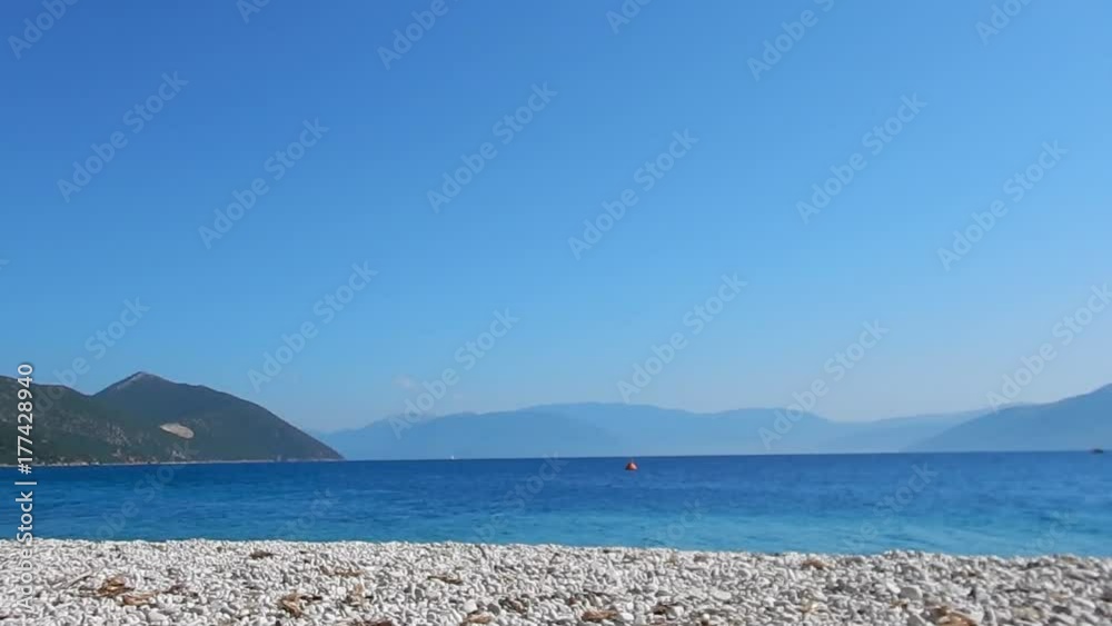 A beach with white stone, turquoise sea, blue sky and mountains in background in Ithaca island in Greece. Copy space. A beach with white stone, turquoise sea, blue sky and mountains in background in Ithaca island in Greece. Copy space.