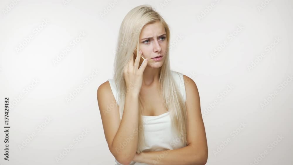 irritated girl with blond hair speaking on mobile phone have unpleasant conversation holding cellphone in hand arguing over on white background. Concept of emotions irritated girl with blond hair speaking on mobile phone have unpleasant conversation holding cellphone in hand arguing over on white background. Concept of emotions
