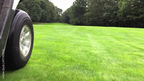 Golf cart driving down fairway on a beautiful golf course during summer day time. Low angle POV driving plate point of view to wheels rolling on grass