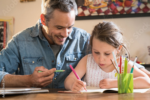 A father helps his little daughter to do her homework for the school.