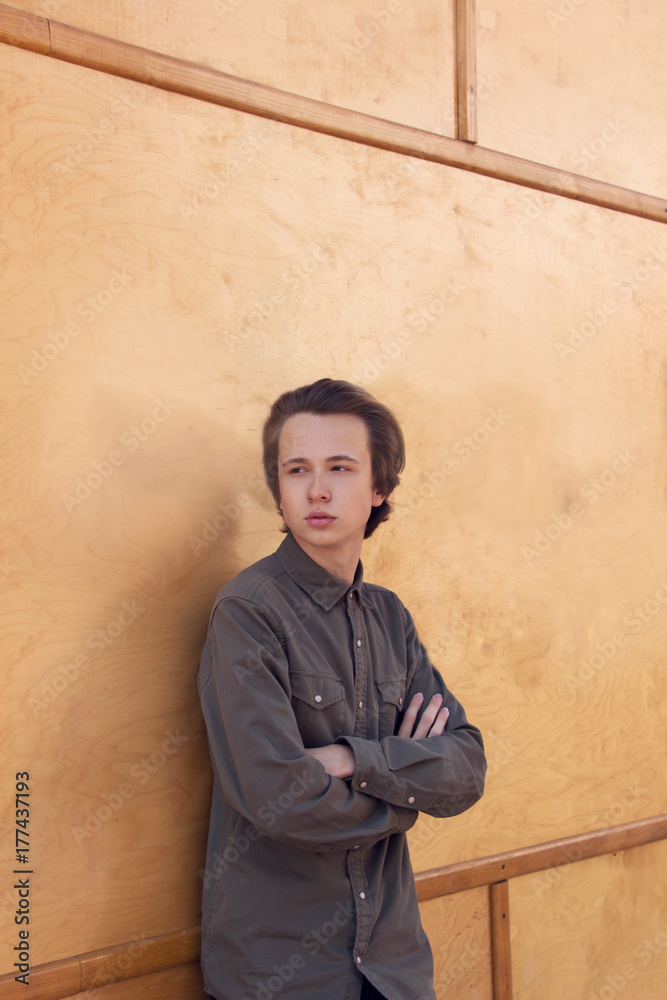 Pensive   Teenage boy standing   near a wooden  wall