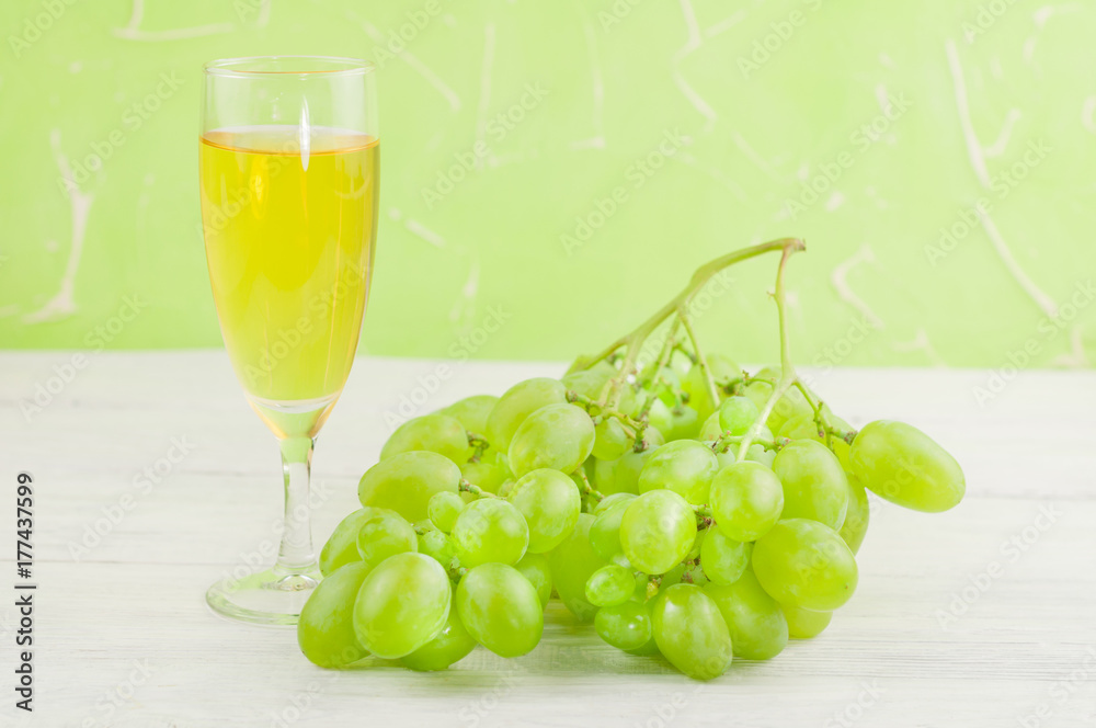 Bunch of fresh ripe green grapes near transparent and fragile glass full of wine on old wooden rustic white planks Bunch of fresh ripe green grapes near transparent and fragile glass full of wine on old wooden rustic white planks