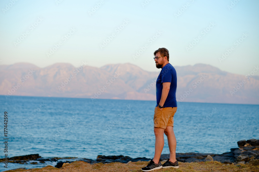 young man stands on the beach around the mountain