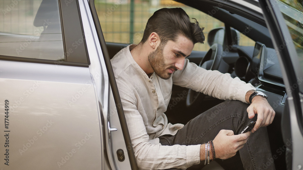 Handsome Young Man using mobile phone while sitting in a car with door open