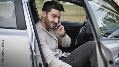 Handsome Young Man talking on mobile phone while sitting in a car with door open © starsstudio