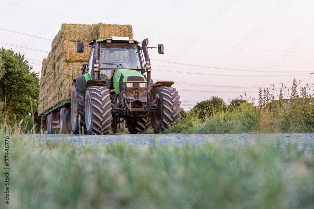 Obraz premium Grüner Traktor mit Anhänger, voll beladen mit Strohballen, Froschperspektive