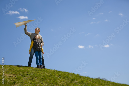 Portrait of man and kid boy sitting on top of hill and going to start paper airplane. Father and son together.