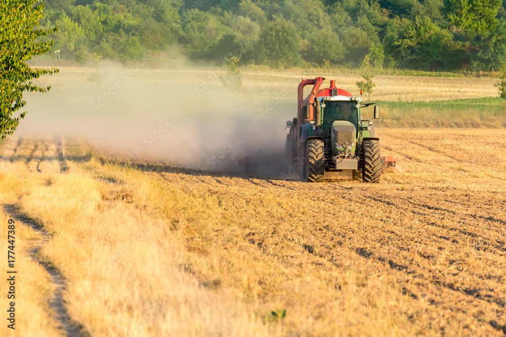 Grüner Traktor mit rotem Anhänger wirbelt eine Staubwolke auf dem Feld auf Grüner Traktor mit rotem Anhänger wirbelt eine Staubwolke auf dem Feld auf