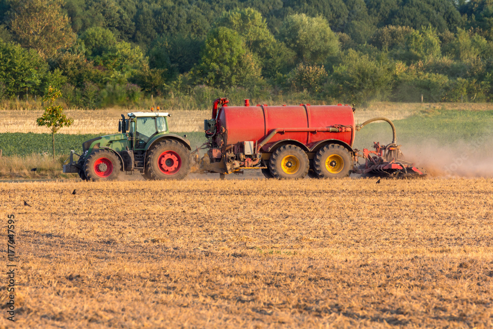 Grüner Traktor mit einem roten Anhänger voller Dünger kultiviert ein Feld,  Freiraum unten Stock-Foto | Adobe Stock