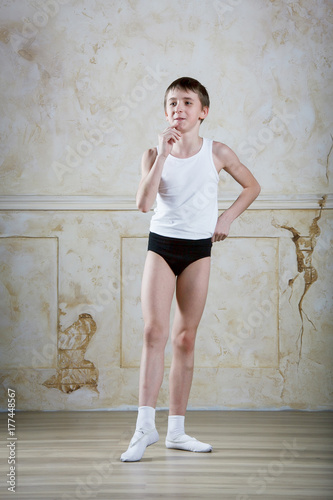 Little ballet caucasian boy dancing in a studio in white shirt and black underpants ballet uniform. Full-length portrait.
