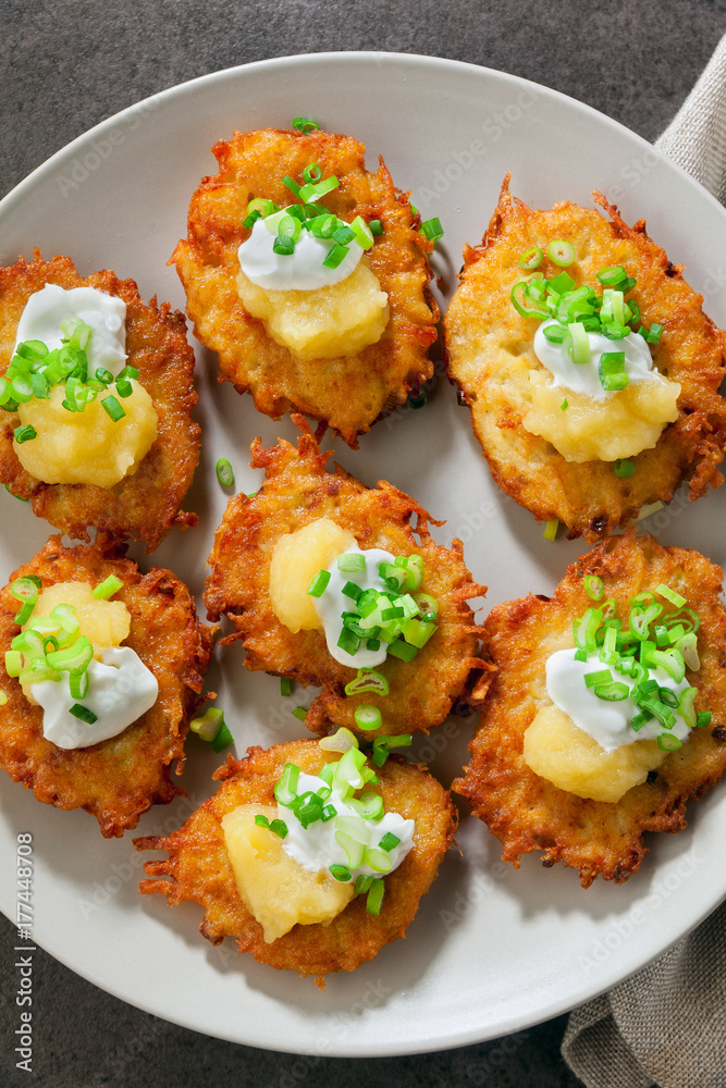 Potato pancakes, latkes or boxty and sauces from sour cream, yogurt, apple sauce and finely chopped green onion on grey stone background Potato pancakes, latkes or boxty and sauces from sour cream, yogurt, apple sauce and finely chopped green onion on grey stone background