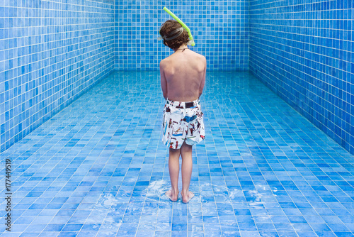 Boy stands in an empty blue swimming pool waiting for the water level to rise photo