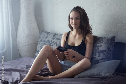 Attractive brunette caucasian woman in home wear, sit at the bed, play video-games with game-pad, look at TV screen with different emotions © morozov_photo