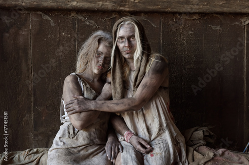 A scene of poverty with two young people. They are seen to be situated in a poor unclean environment wearing rags as clothing. Their faces reveals sadness and sorrow in them.
