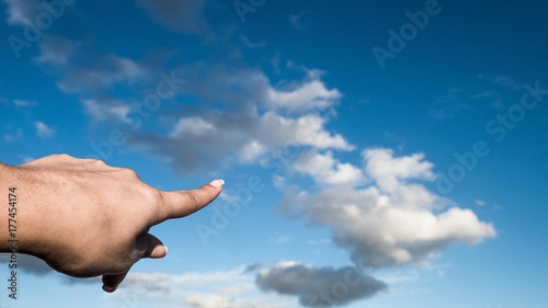 Human finger pointing at cloud in the sky
