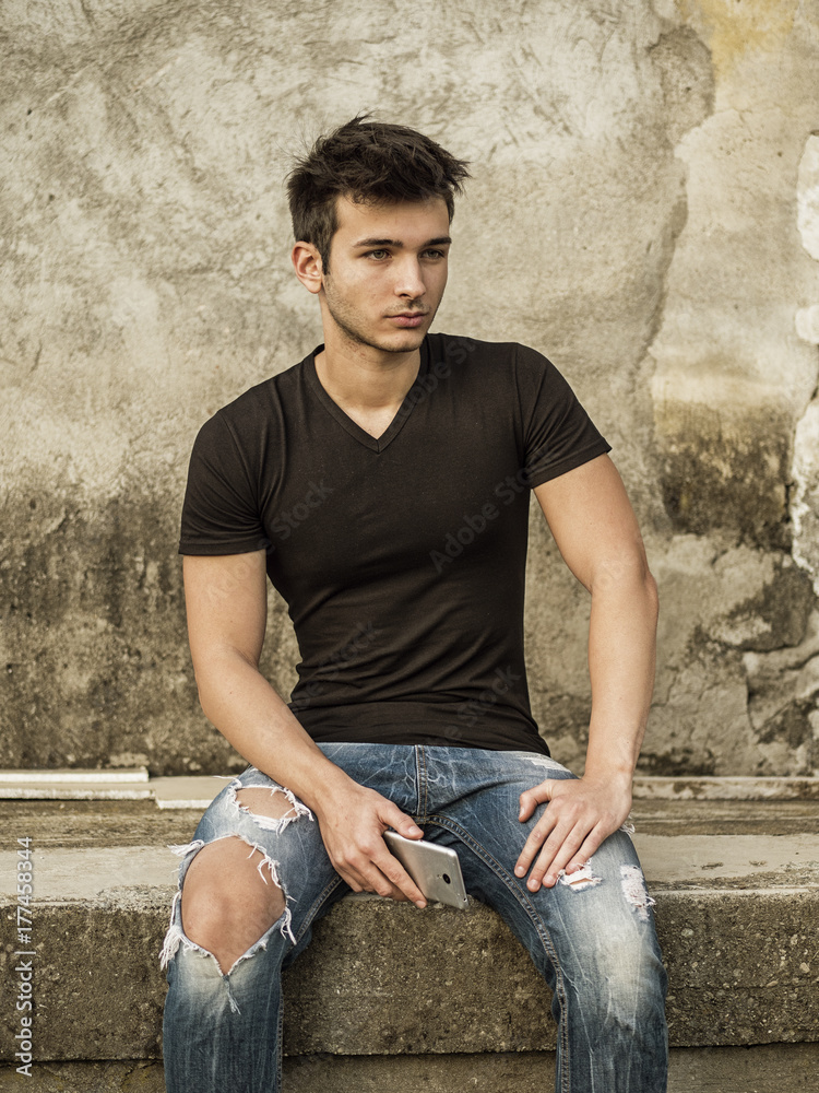 Smiling young man sitting on concrete steps. Arms resting on thighs Smiling young man sitting on concrete steps. Arms resting on thighs